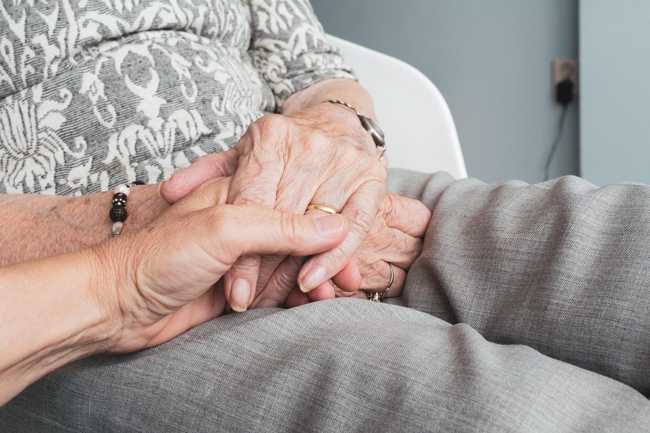 A carer gently holding an elderly person's hands